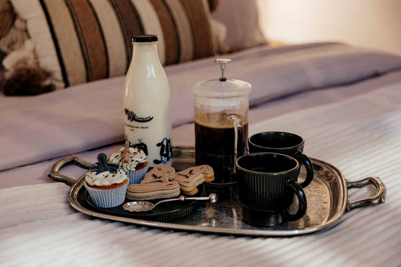 A tray with a milk bottle, a coffee pot, two cups, a cupcake, and a pair of shoes.
