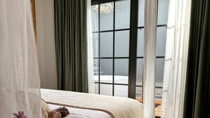Une chambre à coucher avec un cadre de lit en bois, du linge de lit blanc et des rideaux légers.