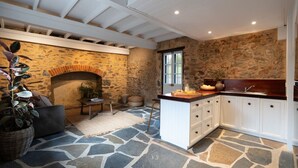 A kitchen with stone walls, a stone floor, white cabinets, and a wooden countertop.