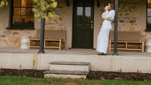 A stone building with a dark door, a covered porch, and a person standing on the porch.
