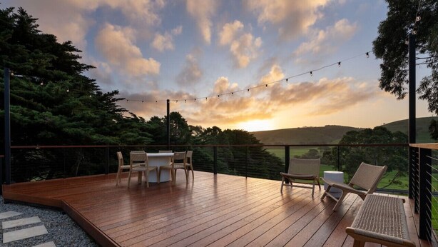 A wooden deck with outdoor furniture, string lights, and a view of the landscape.