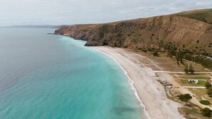 A coastal landscape with a beach, cliffs, and a row of parked vehicles.