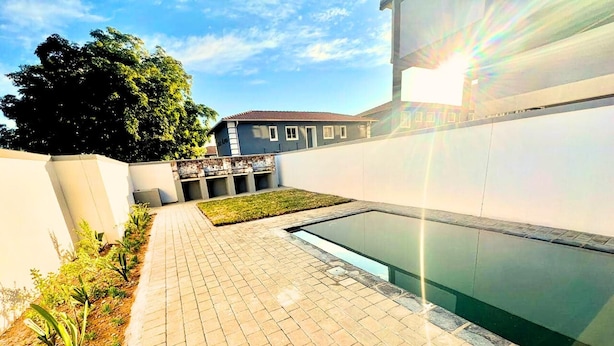 Una piscina con solárium de baldosas, rodeada por un muro bajo y una zona verde.