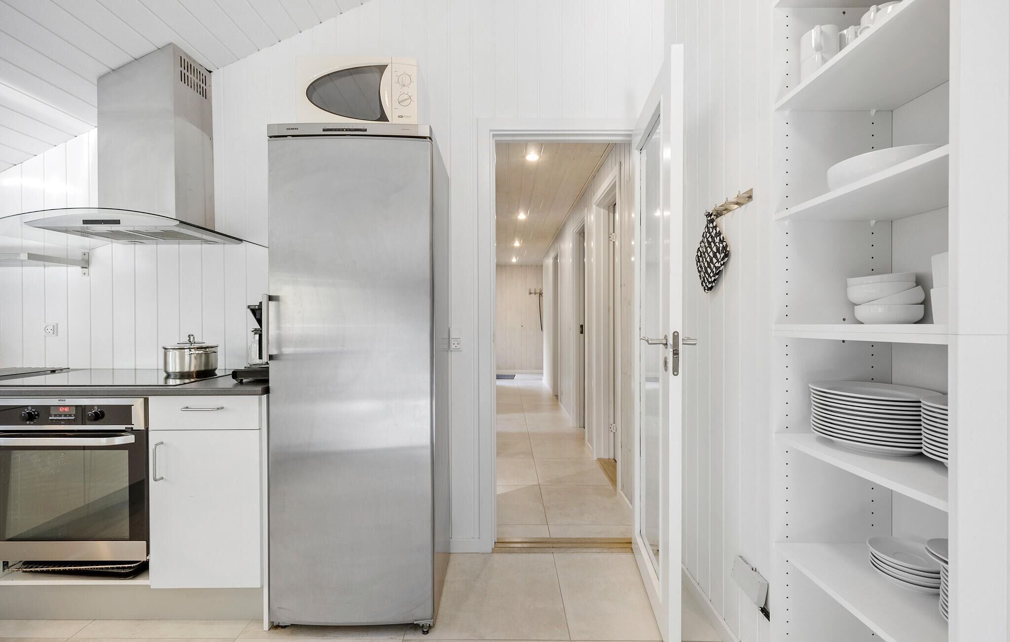 A modern kitchen with a stainless steel refrigerator, oven, and microwave. There are white cabinets and a tiled backsplash.