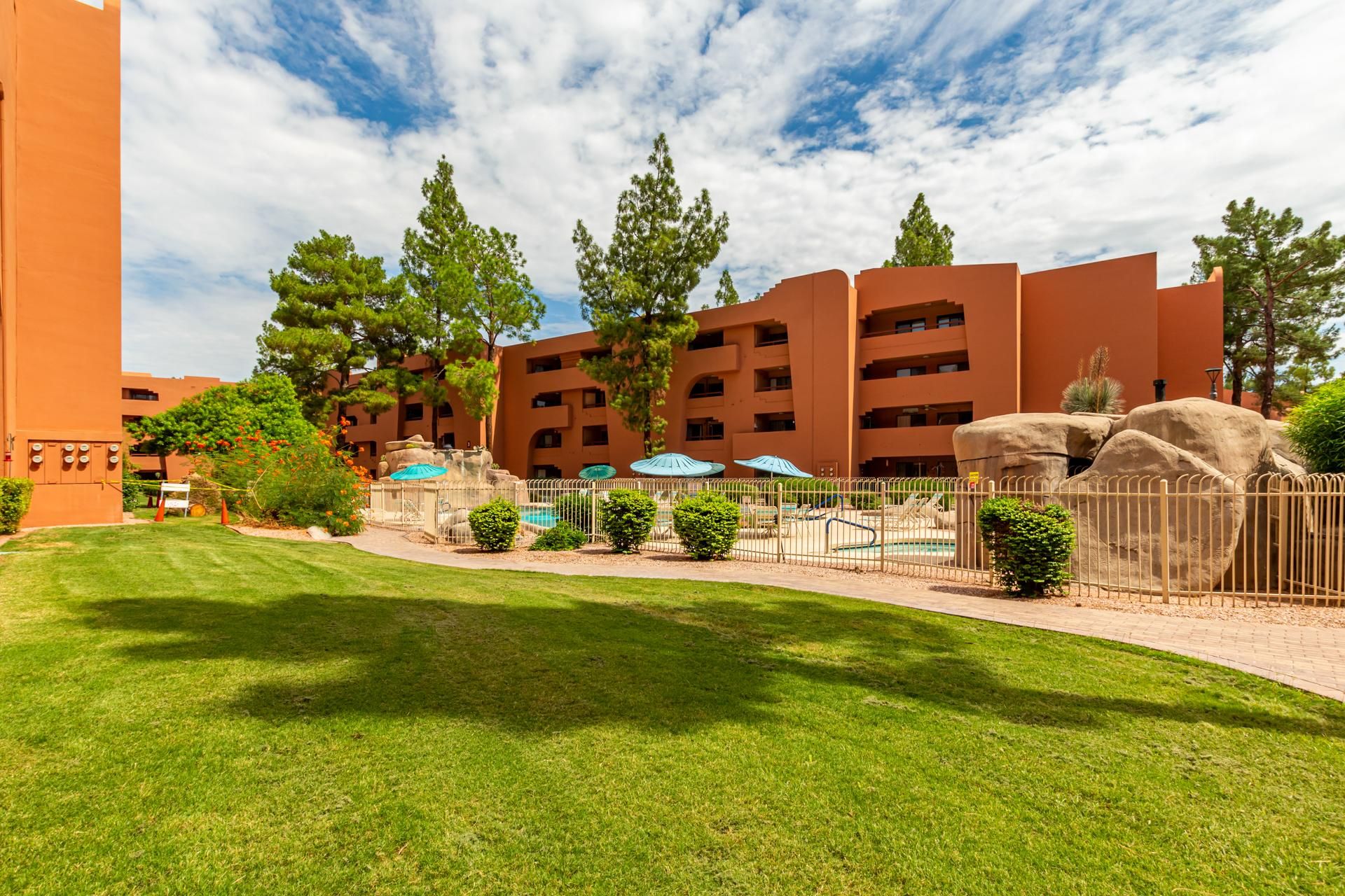 A hotel with a modern orange facade, multiple balconies, and a well-maintained lawn with trees and shrubs.