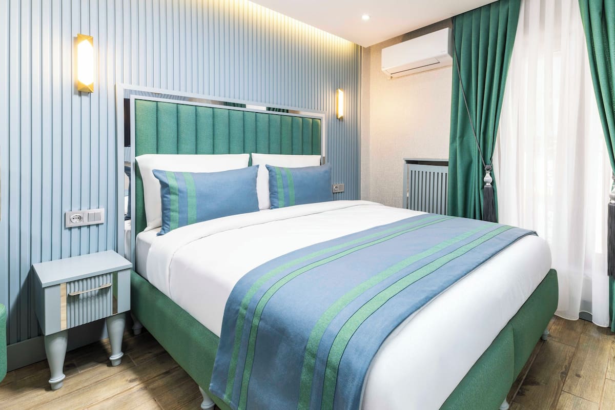 A modern bedroom with a bed, bedside tables, an air conditioning unit, and a window with curtains.