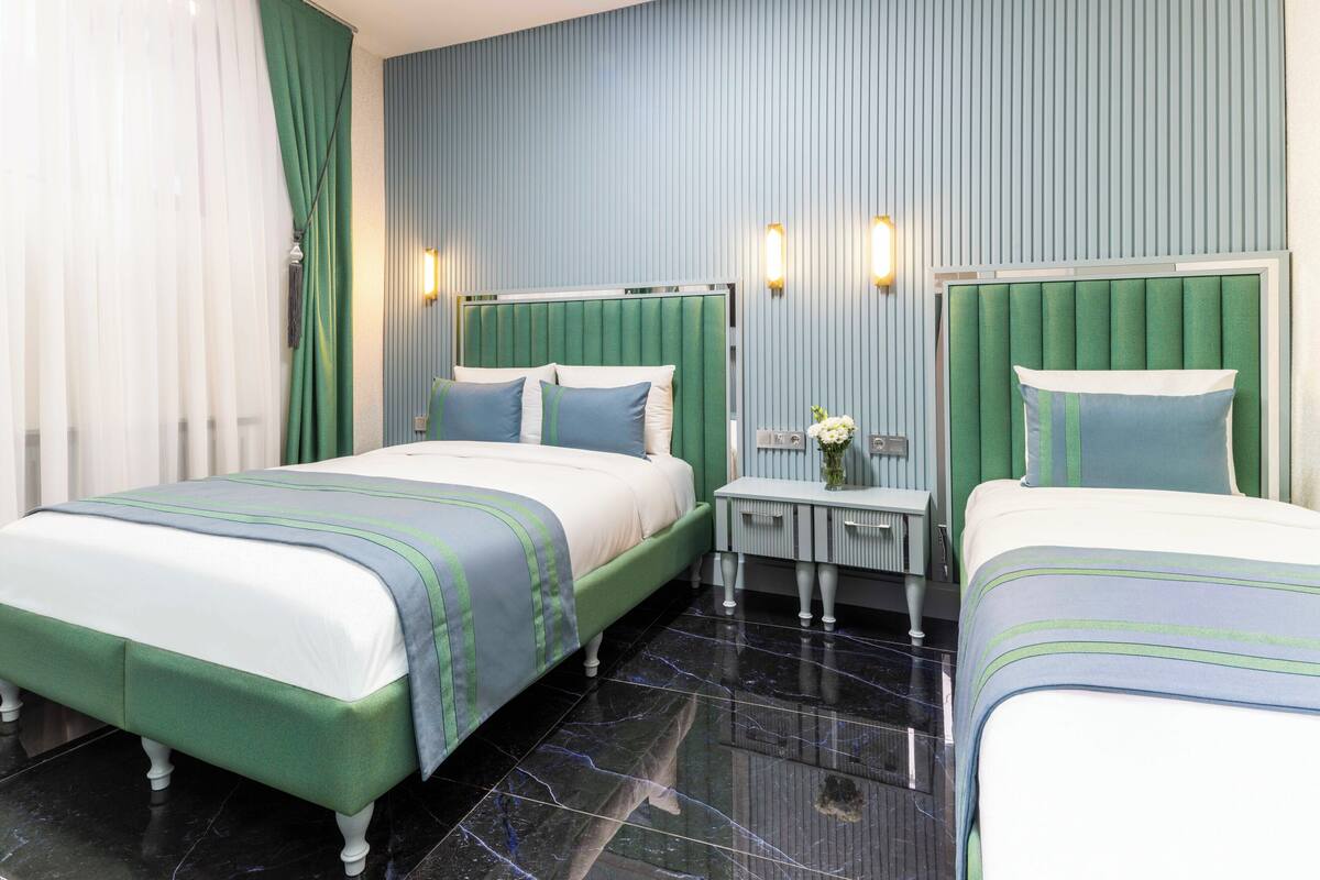 A hotel room with two beds, a nightstand, a mirror, and a window with curtains.