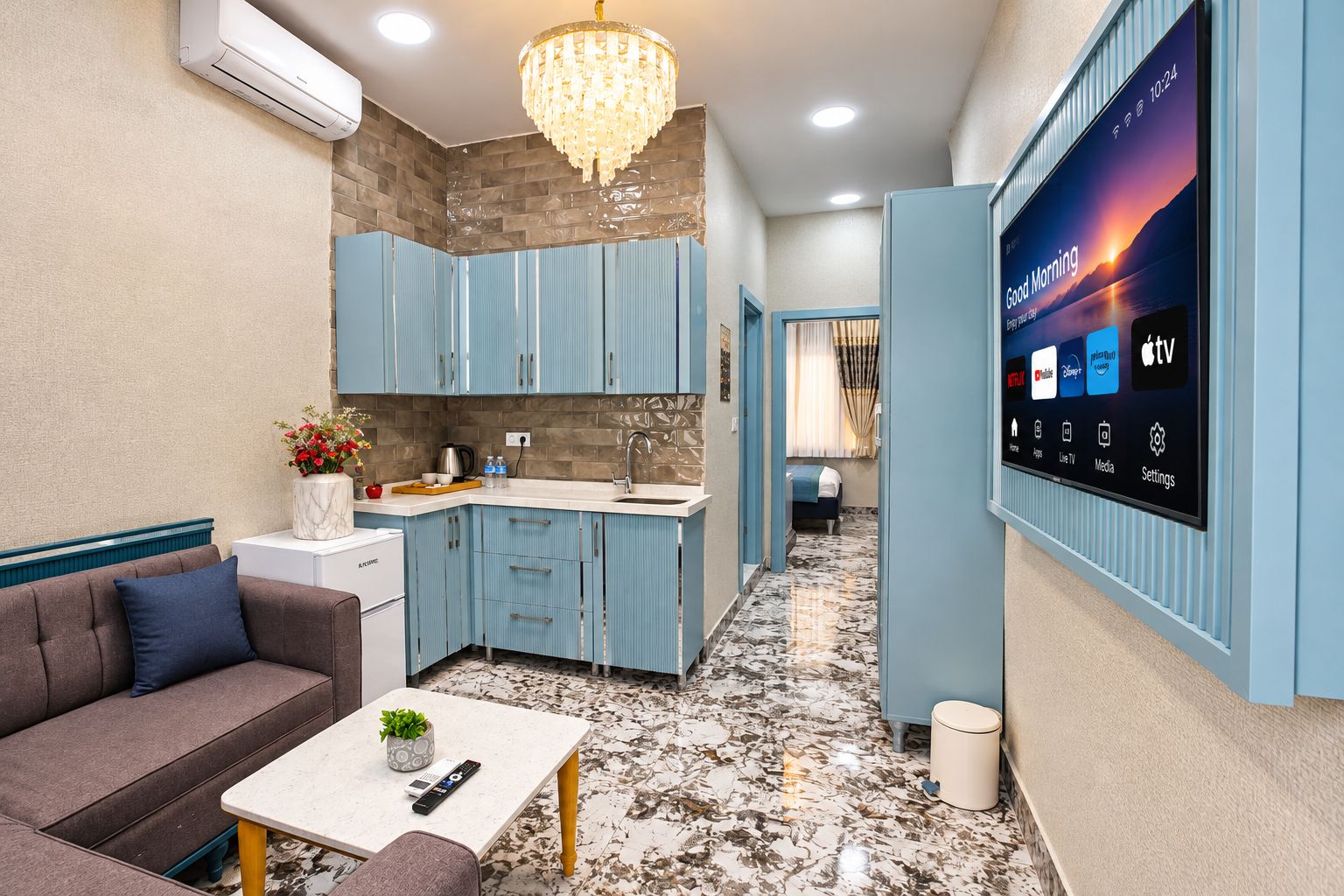 Una cocina moderna con armarios azules, piso de mármol y un televisor montado que muestra varios canales.