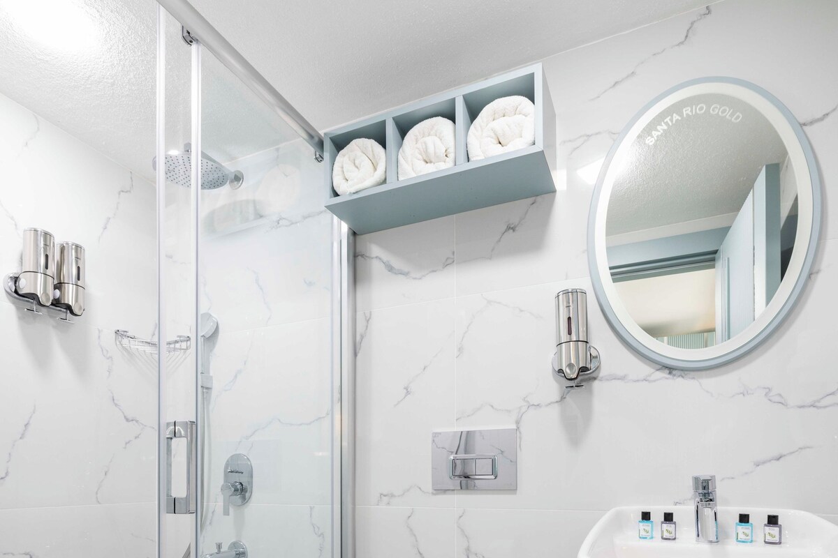 A bathroom with a glass-enclosed shower, a white toilet, a white sink, and a marble-patterned wall.