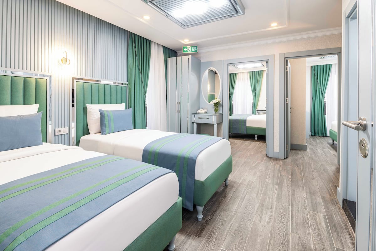 A hotel room with two beds, a vanity with a mirror, and a door leading to another room.