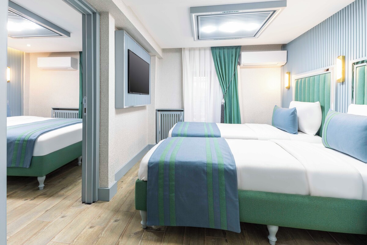A hotel room with two beds, a flat-screen TV, a ceiling fan, and a window with curtains.