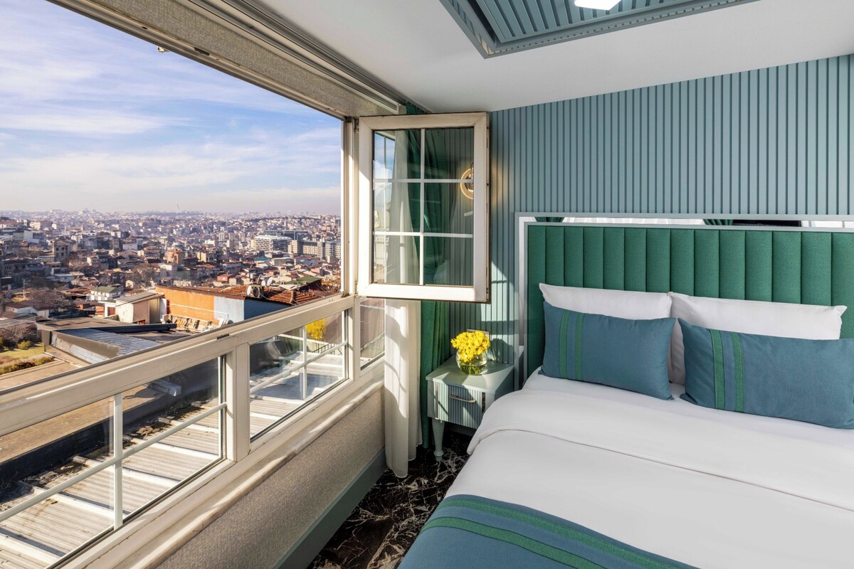 A hotel room with a city view, a large bed, and a window with curtains.