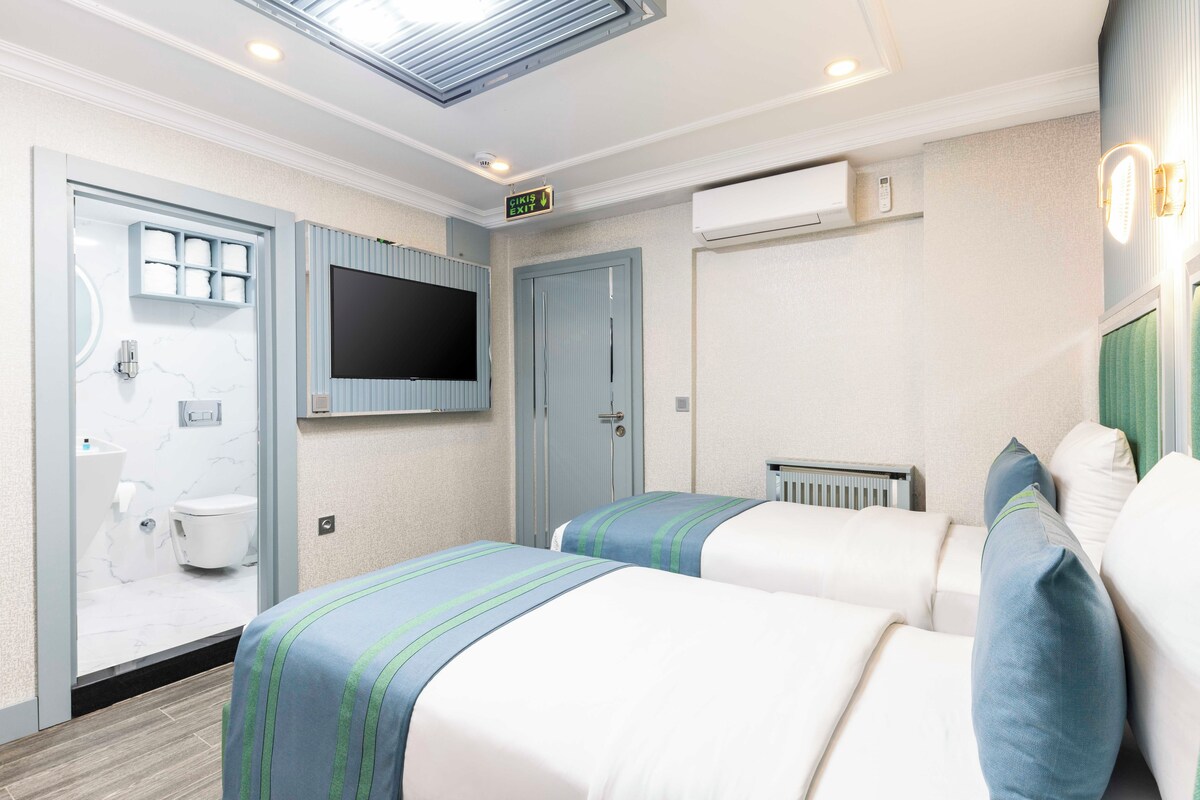 A hotel room with two beds, a TV, a bathroom, and an exit sign.