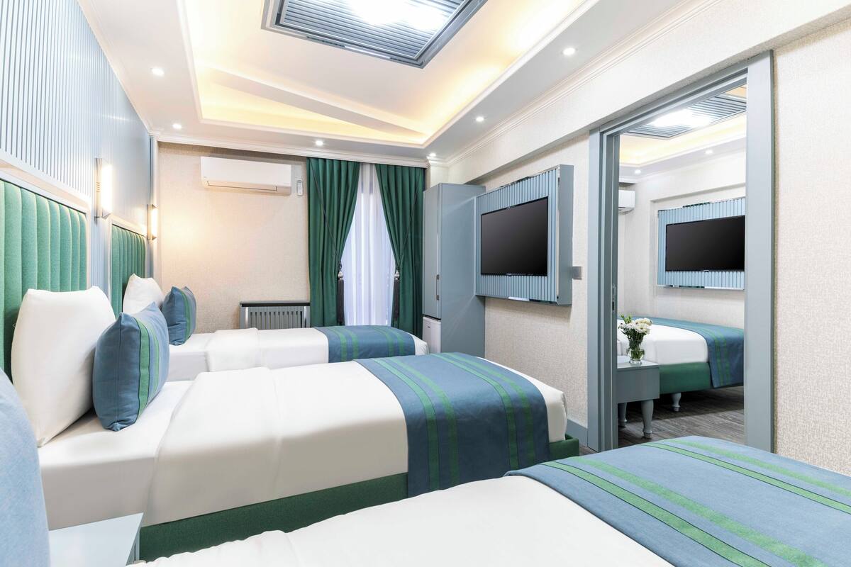 A hotel room with two beds, a TV, a mirror, and a window with curtains.