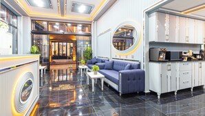 A modern lobby with a reception desk, a blue sofa, a round mirror, and a kitchen area. - Santa Rio Gold Taxim (Istanbul)