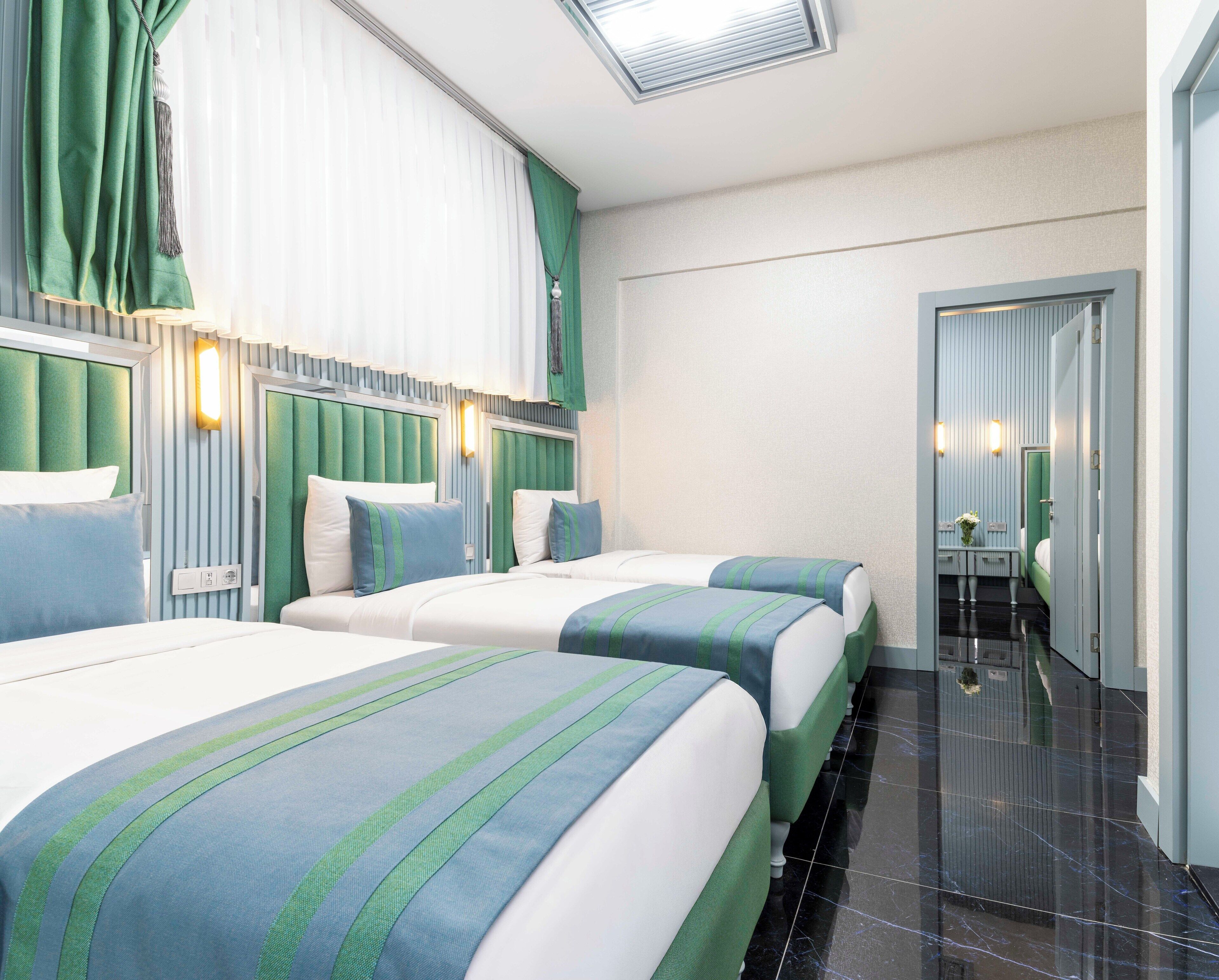 Habitación de hotel con dos camas, cortinas verdes, una mesita y un espejo.