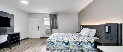 A modern hotel room with a bed, a desk, a chair, a TV, and a window with curtains.