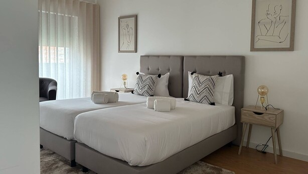 A modern bedroom with two beds, a nightstand with a lamp, and artwork on the walls. - Urban Views Duplex Apt Inspired by Casa da Música (Porto)