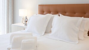 A neatly made bed with white linens and pillows, a bedside lamp, and a brown upholstered headboard.