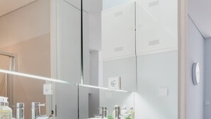 A modern bathroom with two sinks, a large mirror, and a walk-in closet.