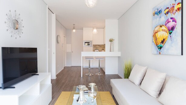 A modern living room with a flat-screen TV, white sofa, and a painting of hot air balloons.
