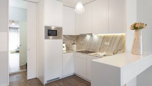 A modern kitchen with white cabinetry, a built-in microwave, a marble backsplash, and a pendant light.