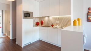 Een moderne keuken met witte kastjes, een magnetron, een spoelbak en een marmeren achterwand. Boven de aanrecht hangen twee hanglampen en staat er een biertje.