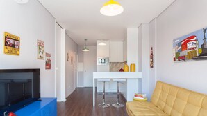 Een moderne woonkamer met een bank, een tv-meubel, een rood vloerkleed en een keukenhoek met een wit aanrecht en barstoelen.
