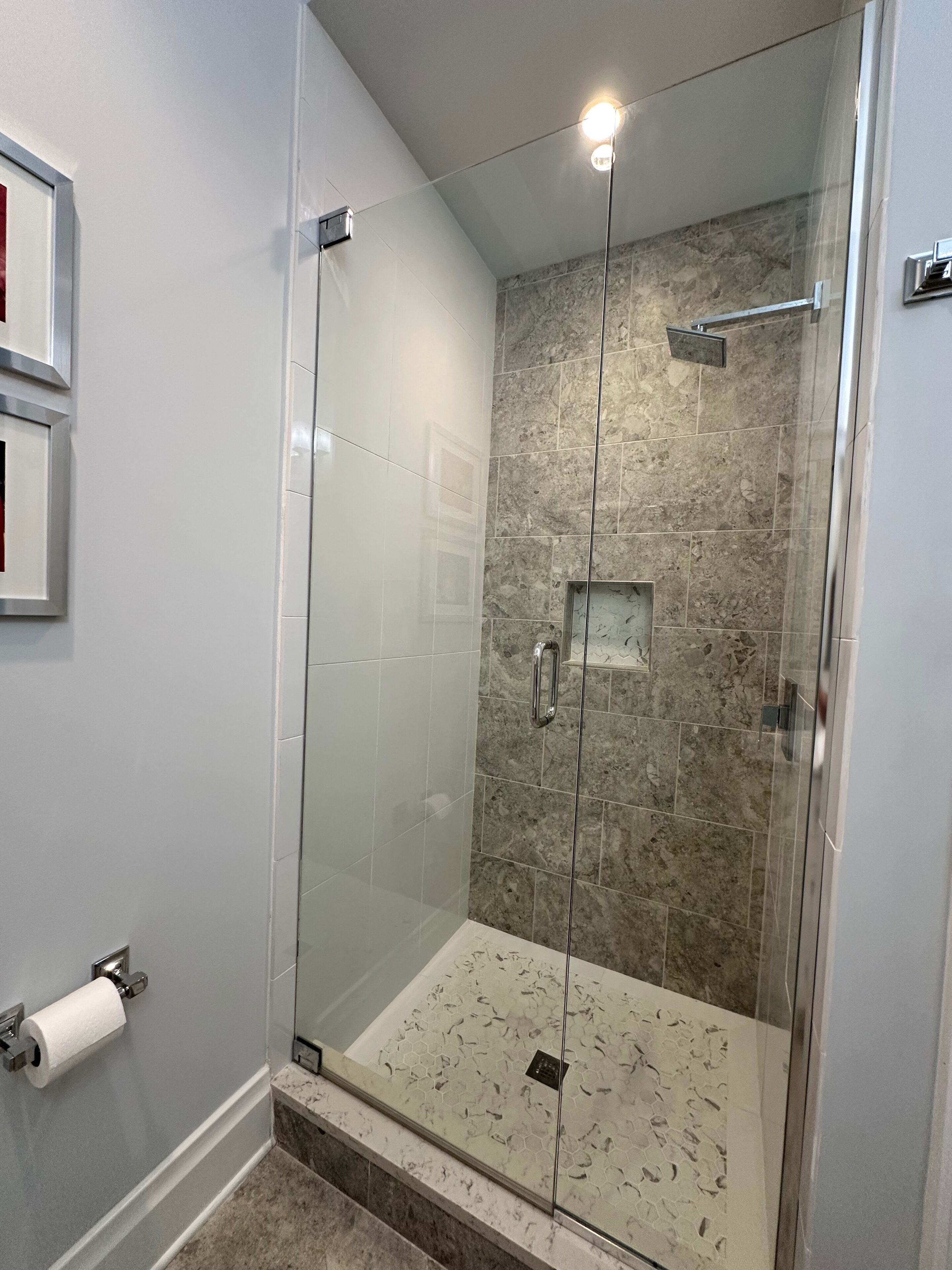 A modern shower with glass doors, a marble shower floor, and a wall-mounted towel dispenser.