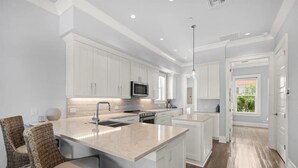 Una cocina moderna con muebles blancos, una isla central y una zona de comedor con sillas de mimbre.
