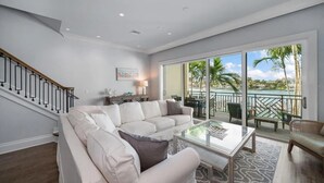 Amplia sala de estar con un sofá blanco, una mesa de centro de vidrio y vistas a un balcón con mobiliario exterior.