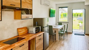 Una cocina moderna con armarios de madera, microondas integrado y refrigerador. Hay una zona de comedor con una mesa y sillas, y un ventanal que ofrece vistas al exterior.
