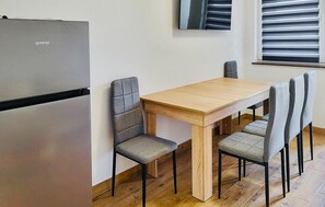 A compact kitchen with a wooden table and four chairs, a built-in refrigerator, and a window with blinds. - 2 bedroom gorgeous home in Pustkowo (Pustkowo)
