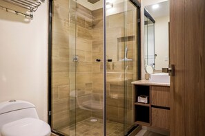 Een moderne badkamer met een douchecabine van glas, een houten wastafelmeubel met spiegel en een toilet.