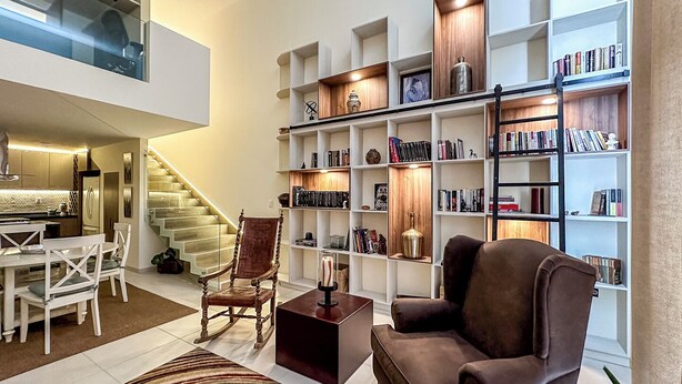 A modern living room with a staircase, a bookshelf, and a dining area.