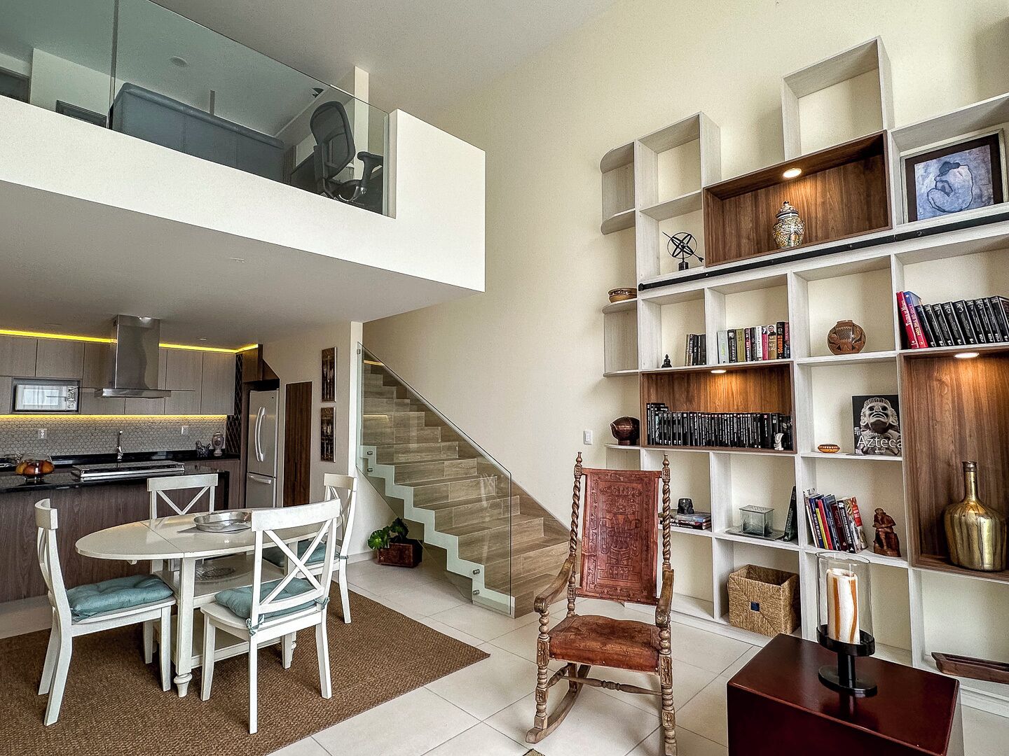 A modern interior with a dining area, a staircase, and a bookshelf.