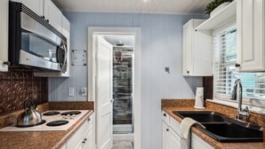 Una cucina compatta con mobili bianchi, un forno a microonde integrato, un piano cottura e un lavello.