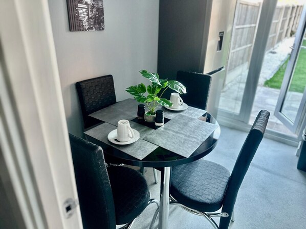 A modern dining area with a glass table, black chairs, and a potted plant. - Luxurious Wolverhampton Retreat With 4 Bedrooms (Wolverhampton)