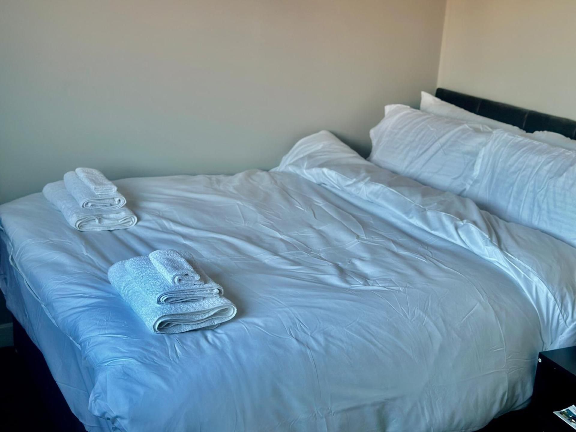 A neatly made bed with white linens and rolled towels.