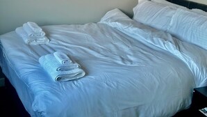 Una cama bien hecha con sábanas blancas y dos toallas enrolladas al lado.