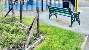 Un parque infantil con un tobogán azul y estructuras para escalar, rodeado por una valla.