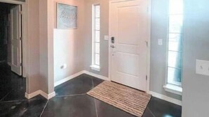 Um corredor com piso de azulejos escuros, uma porta branca e um tapete pequeno.