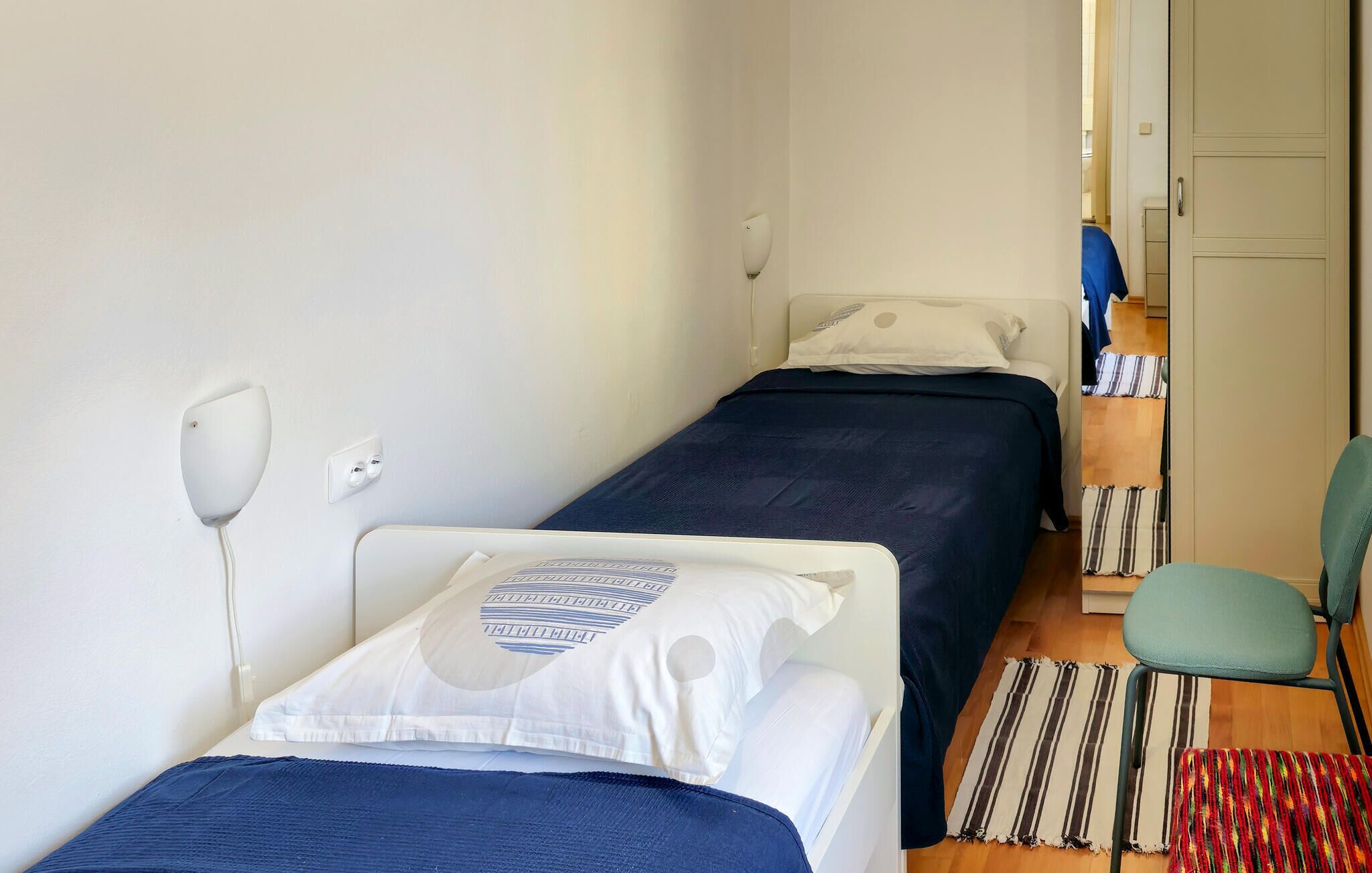 Une petite pièce, de taille modeste, comprenant deux lits simples, un bureau et une chaise.