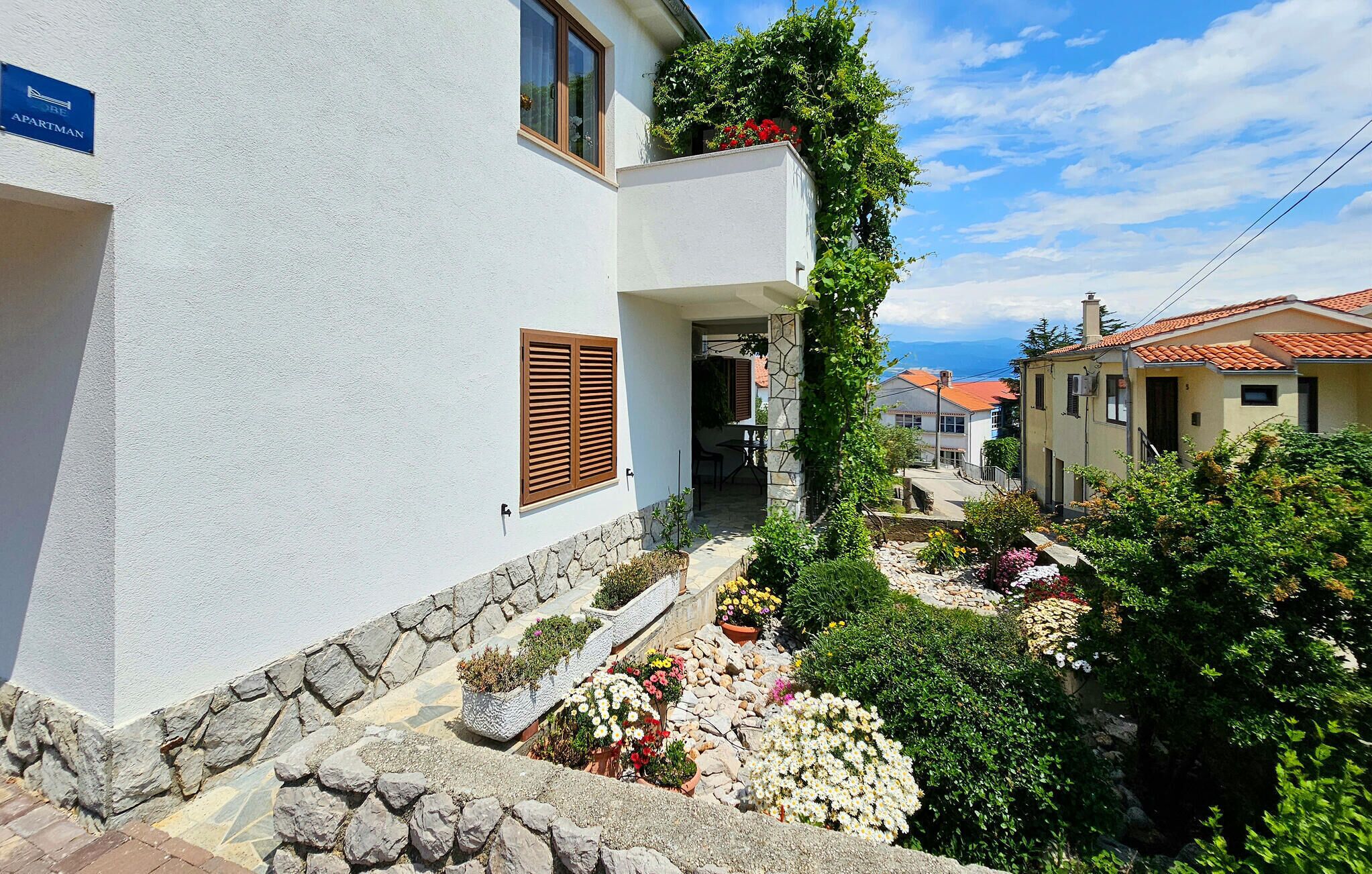 A white building with a stone base, a wooden door, and a sign indicating it's an apartment.