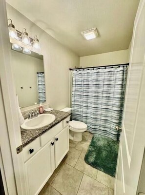 Bathroom features a sink, mirror, toilet, and shower with a striped curtain.