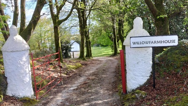 A dirt path leading to a property named Willow Farmhouse, surrounded by trees and a red gate. - Willowfarmhouse Accommodation (Milford)