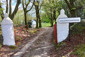 A dirt path leading to a property named Willow Farmhouse, surrounded by trees and a red gate. - Willowfarmhouse Accommodation (Milford)