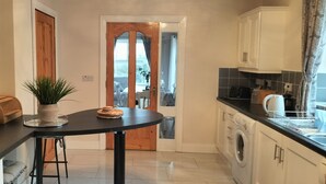 A compact kitchen with a round table, a potted plant, and a wooden door leading to a balcony. - Willowfarmhouse Accommodation (Milford)