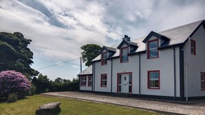 A two-story house with a white exterior and red trim, a front door, and a small porch. - Willowfarmhouse Accommodation (Milford)