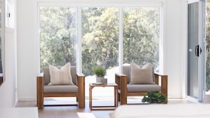 A modern room with two wooden chairs, a small table, and a large window offering a view of trees.